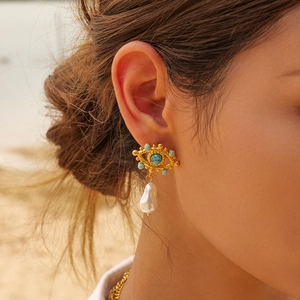 Detail of evil eye gold earrings with turquoise bead and baroque pearl drop on model