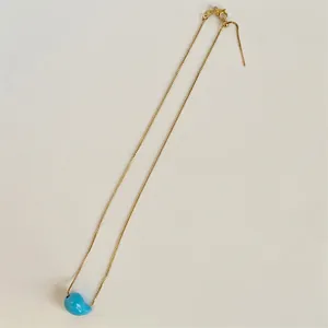 Detail of gold chain necklace featuring a glossy sky blue bean pendant and lobster clasp