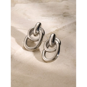 Macro detail of silver intertwined double-loop earrings on a textured stone surface