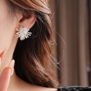 Close-up of sparkling silver firework flower earrings worn by a model in soft focus