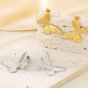 Minimalist gold and silver butterfly stud earrings with textured wings on a stone