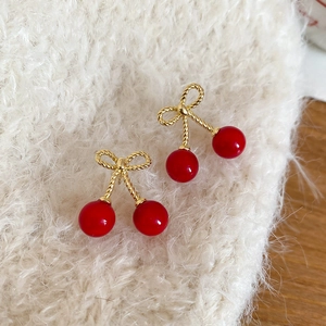 Detailed macro view of cherry bow earrings with red beads on soft white fabric