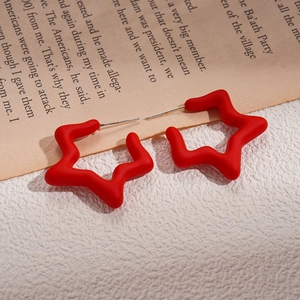 Detail of red frosted star earrings with silver posts on a textured white surface