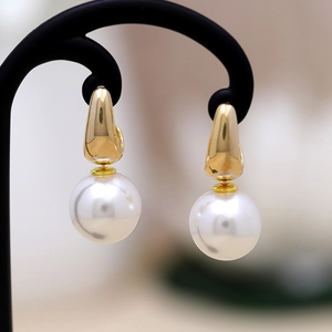 Elegant gold teardrop pearl earrings with polished finish on a black jewelry stand