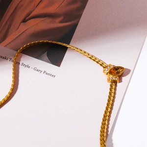 Golden snake chain necklace with amber zircon pendant on magazine background