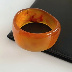 Detail of amber resin bangle featuring internal sand-like texture on a black stand