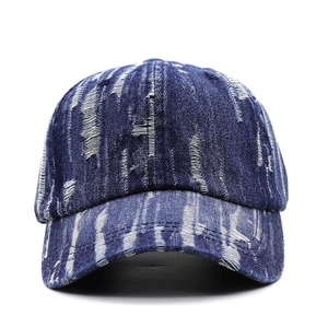 Detailed close-up of distressed dark blue denim baseball cap with frayed hole details