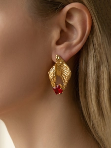 Detailed close-up of a gold conch earring with red zircon and artistic texture
