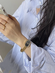 Detail of elegant gold mesh strap watch with oval black dial on a woman's wrist