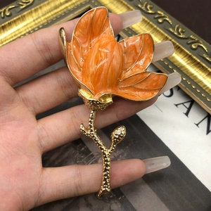 Detail of elegant orange enamel magnolia flower brooch with golden textured petals and stem