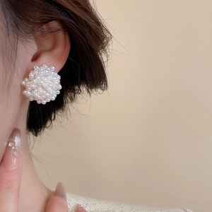Detail view of a luxury white pearl cluster earring worn by a model in warm beige tones