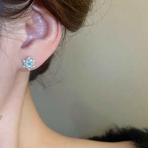 Close-up of elegant silver snowflake earring with blue gemstone on female model