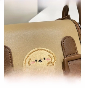Detail show of two-tone leather shoulder bag with a cute plush cartoon patch and stitching