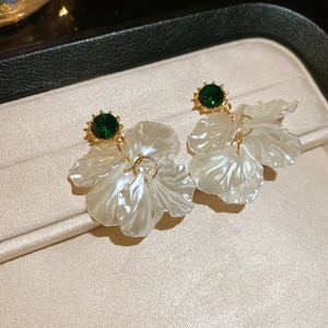 Detailed close-up of elegant flower earrings with green crystals and creamy white petals