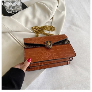 Detail of crocodile pattern shoulder bag featuring golden lion head buckle and metal chain