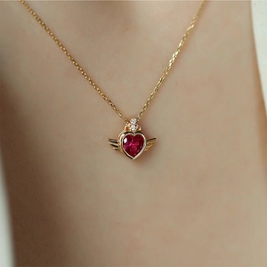 Detail of red heart gemstone necklace with gold wings pendant worn by a model