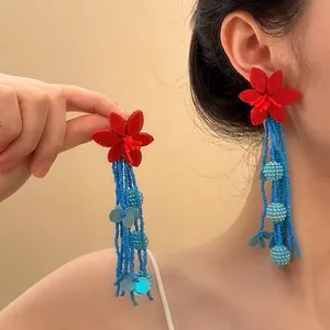 Détail de boucles d'oreilles bohèmes avec fleurs en tissu rouge et perles bleues