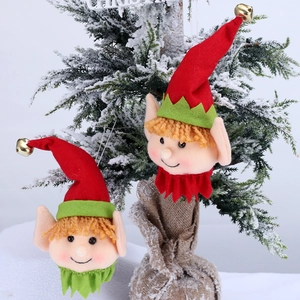 Detail of felt Christmas elf head ornaments with gold bells hanging on frosted pine tree