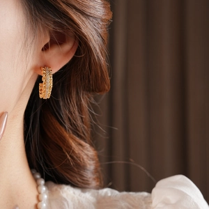Detail of 18k gold plated C-shaped earring with sparkling rhinestones on model's ear