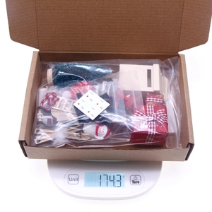 Overhead view of miniature Christmas dollhouse set in a box on a digital scale weighing 174.3g
