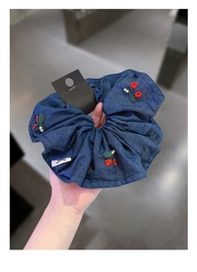 Detail of blue denim scrunchie with red cherry embroidery and elegant pearl accents