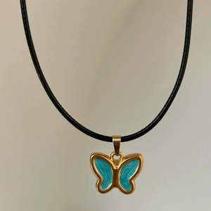 Detailed view of 18k gold plated butterfly pendant with blue enamel on a black cord
