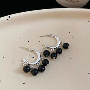 Detailed macro view of silver C-shape earrings with hanging black bead tassels on a tray