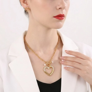 Gros plan sur une parure de bijoux cœur dorés avec collier à fermoir OT et boucles d'oreilles