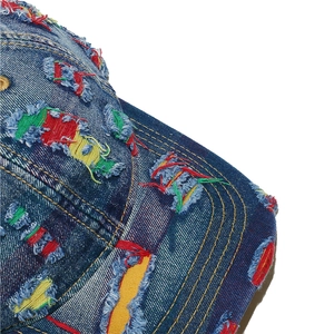 Dettaglio ravvicinato del cappellino in denim invecchiato con toppe colorate e strappi