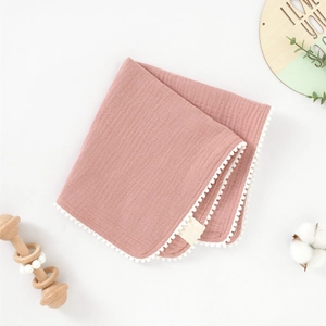 Détail d'une serviette carrée pour bébé en coton doux avec dentelle à pompons blancs