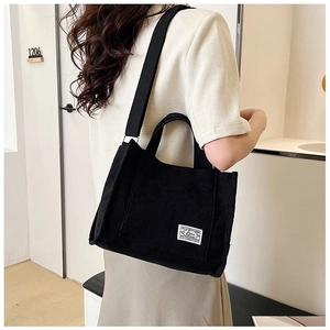 Detail view of black corduroy tote bag featuring adjustable strap and white woven label