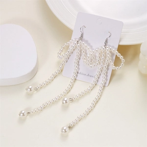 Elegant white pearl bow earrings with long tassels on a minimalist ceramic plate