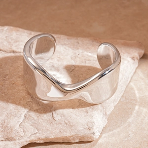 Close-up of a silver polished wide cuff bracelet with wavy edges on a stone surface