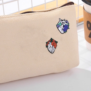 Artistic enamel heart brooches with blue and red flowers pinned on a beige canvas bag