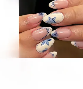 Detailed view of almond-shaped press-on nails with blue floral patterns and ribbon art