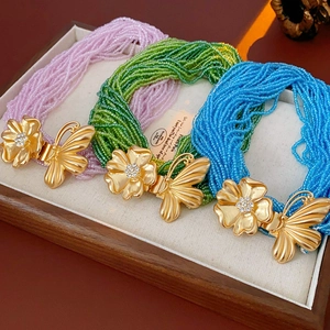 Macro detail of multilayer beaded necklace with crystal butterfly and gold flower charms