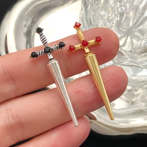 Gothic sword earrings with crystal accents in silver and gold displayed on fingers