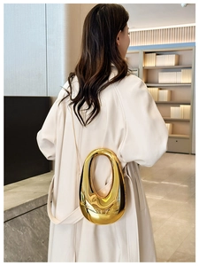 Polished gold streamlined metal handbag with thin chain strap carried by a model