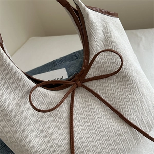 Large white woven tote bag with brown leather bow and herringbone texture for summer commuting