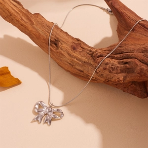 Detail of a silver-tone 3D bow pendant with snake chain draped on natural wood