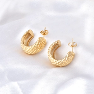 Macro detail of gold-plated C-shaped earrings with quilted texture on white silk fabric
