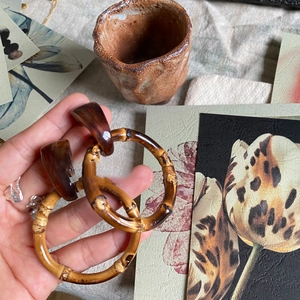 Detail shot of vintage resin and bamboo hoop earrings held by hand over rustic decor