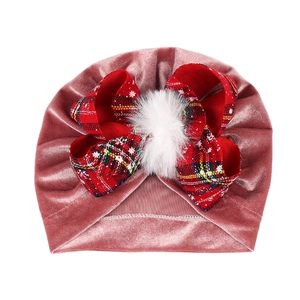 Detail of pink velvet baby turban with red plaid bow and white faux fur pompom
