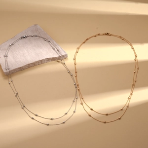 Minimalist gold and silver satellite chains with oval beads on stone in striped shadow