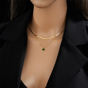 Gold double layer necklace with green square pendant and flat snake chain on black suit