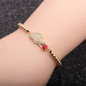 Macro shot of gold zircon bracelet featuring heart and hand gesture charms on model