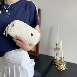 Detail of hand-held cream quilted makeup bag with embroidered bow and ribbon zipper