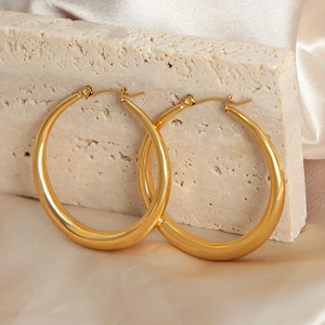 Polished gold-plated large hoop earrings displayed on stone with silk backdrop