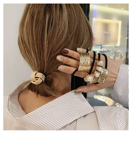 Close-up of three gold metal hair ties including a twist knot, wide band, and pearl charm style
