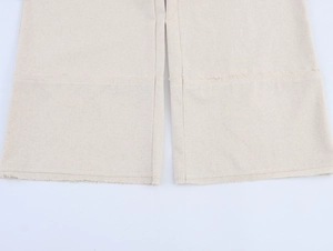 Detail view of beige linen-style pants featuring stitched seams and raw fringe hemline